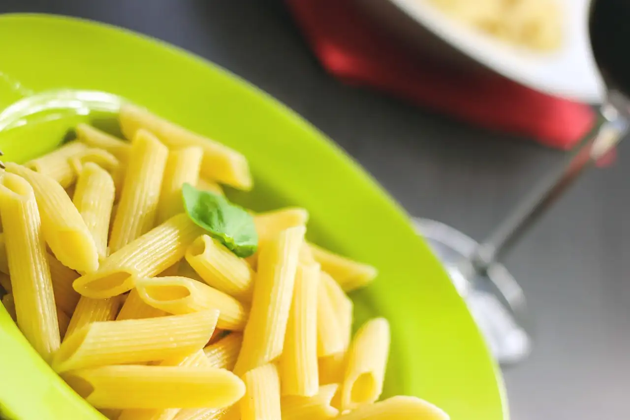 Assiette de penne au basilic servie sur une table de restaurant, verre à pied en arrière-plan