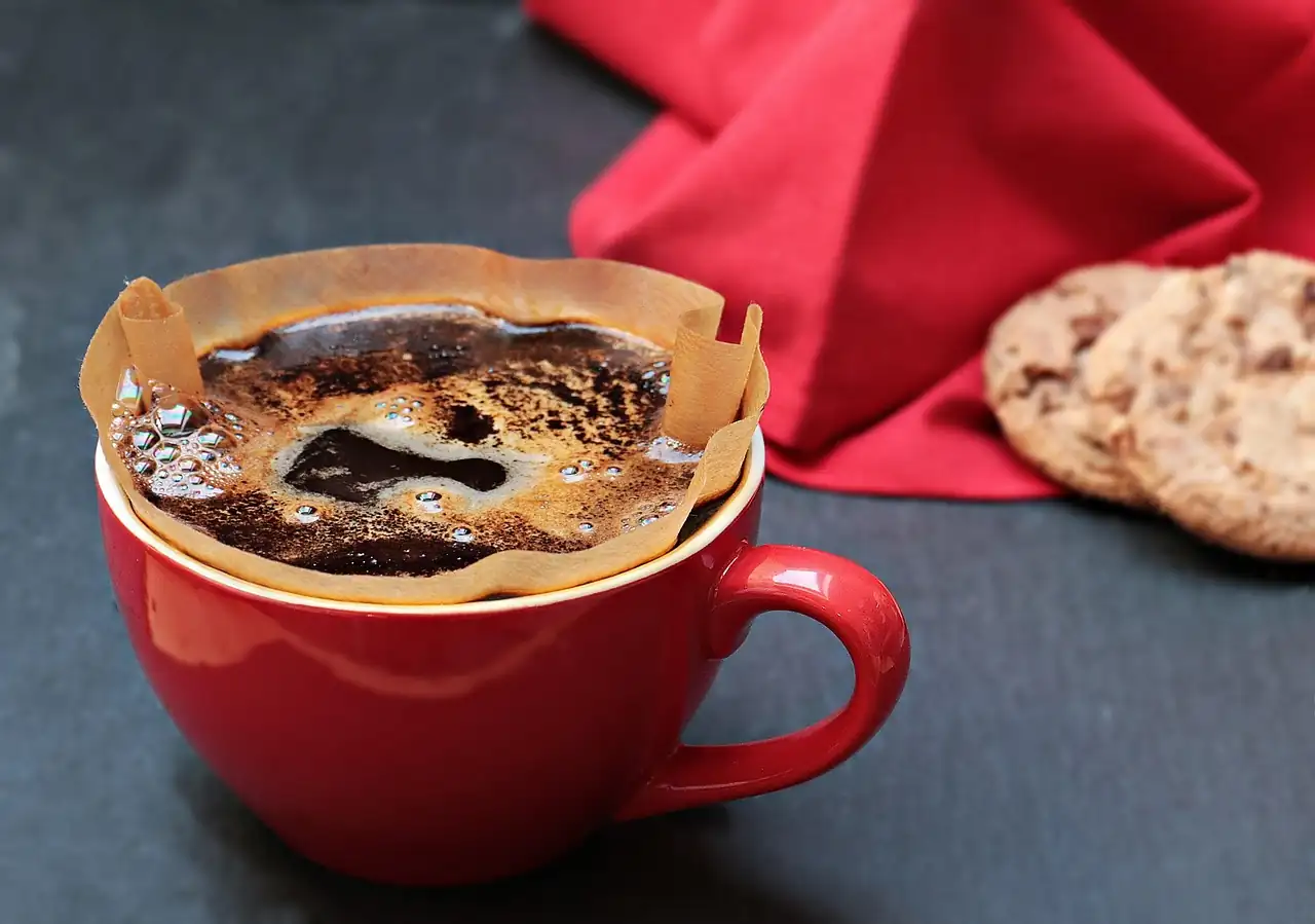 Café filtre en train de passer dans un mug rouge, serviette rouge et biscuits flous en arrière-plan