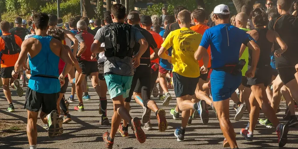 Peloton de coureurs amateurs vus de dos sur une allée boisée, hommes et femmes de tous âges
