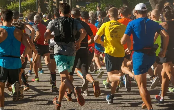 Peloton de coureurs amateurs vus de dos sur une allée boisée, hommes et femmes de tous âges