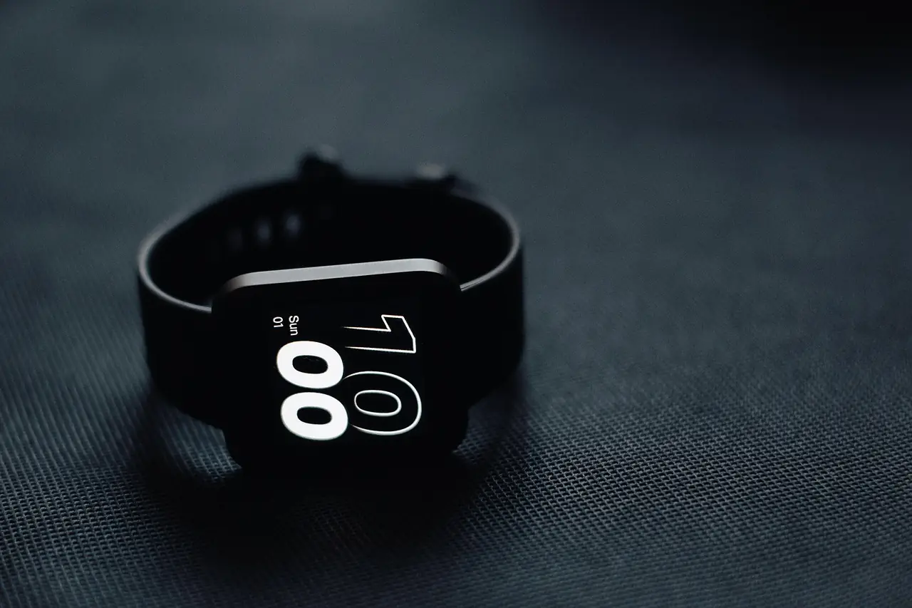 Montre connectée noire posée sur un tissu sombre, écran allumé affichant l'heure