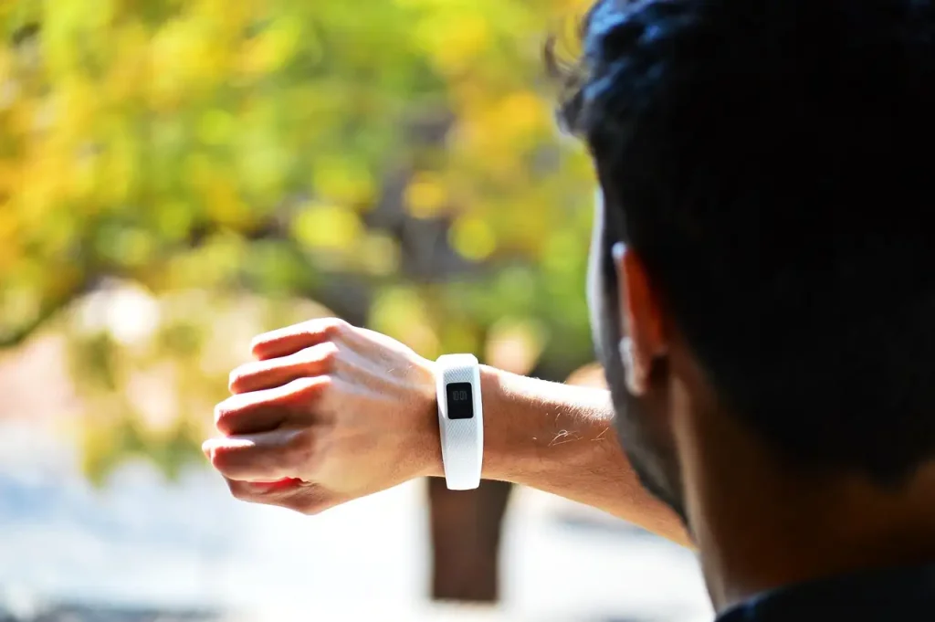 Homme vu de dos qui consulte le bracelet connecté à son poignet, feuillage d'automne flou en arrière-plan