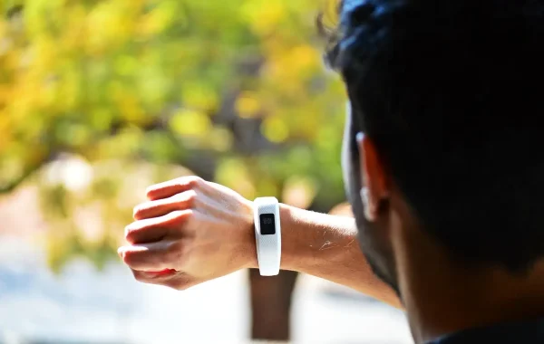 Homme vu de dos qui consulte le bracelet connecté à son poignet, feuillage d'automne flou en arrière-plan