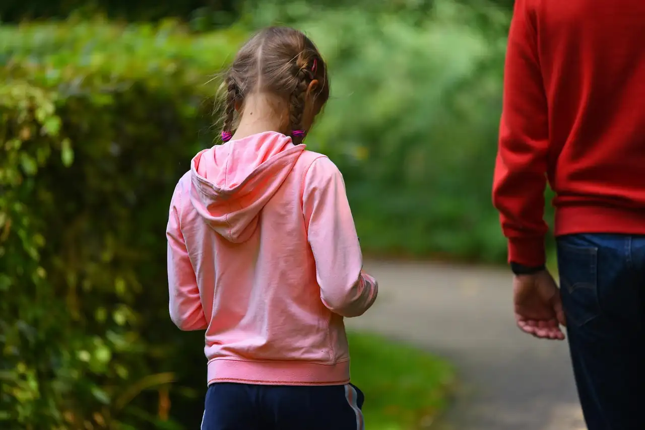 Fillette en sweat rose à capuche qui marche sur un chemin en tenant la main d'un adulte