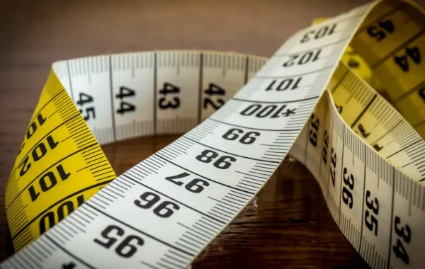 Mètre ruban de couture jaune et blanc déroulé en gros plan sur une table en bois