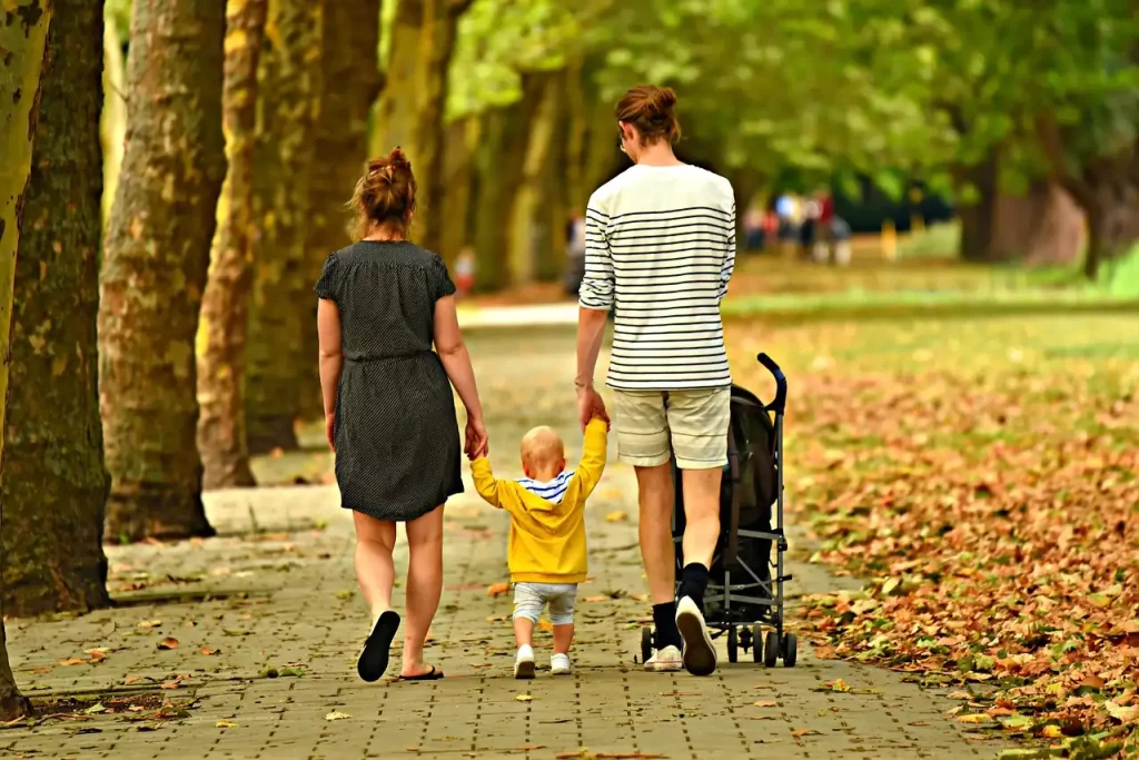 Parents marchant de dos dans une allée de parc en automne, un jeune enfant entre eux et une poussette