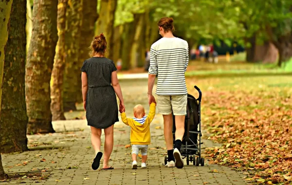 Parents marchant de dos dans une allée de parc en automne, un jeune enfant entre eux et une poussette