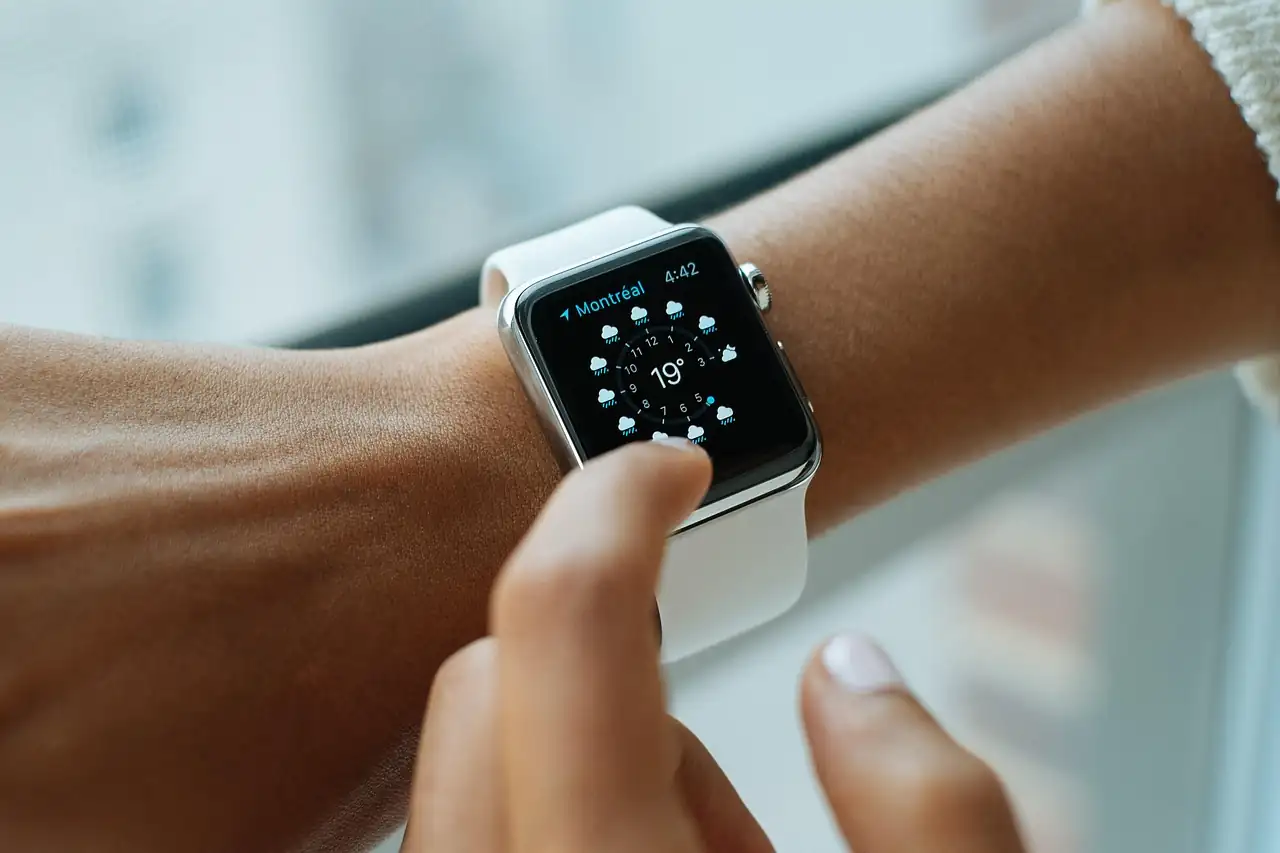 Montre connectée blanche au poignet, écran météo affiché, doigt posé sur le cadran