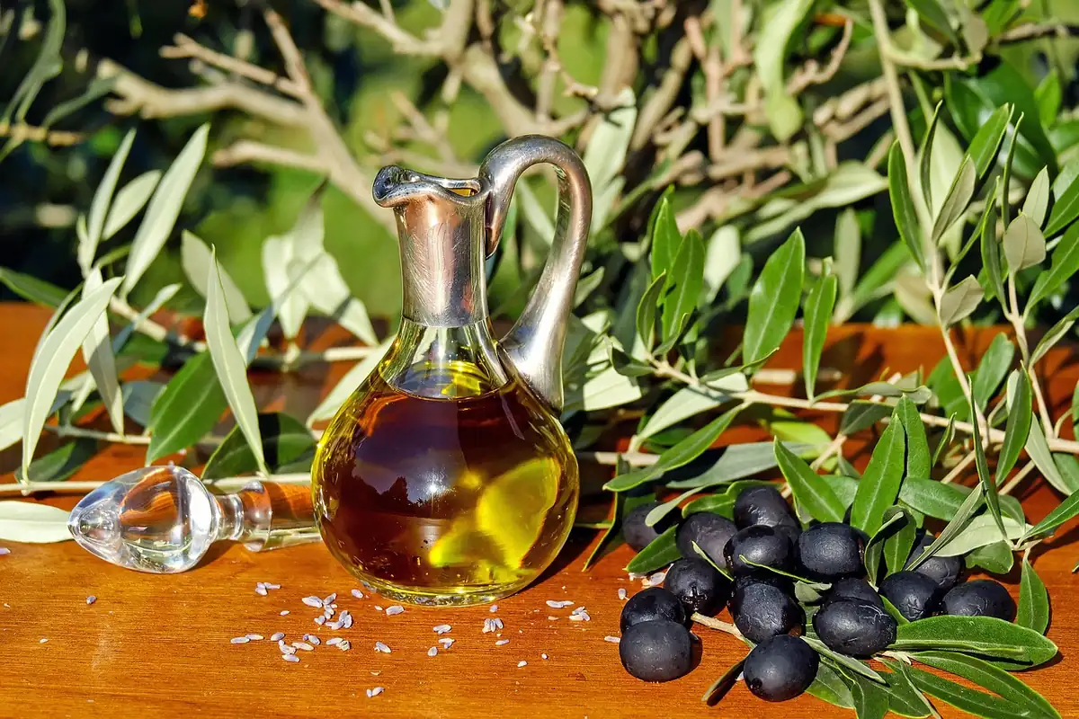 Carafe en verre d'huile d'olive posée sur une table en bois, olives noires et branches d'olivier autour
