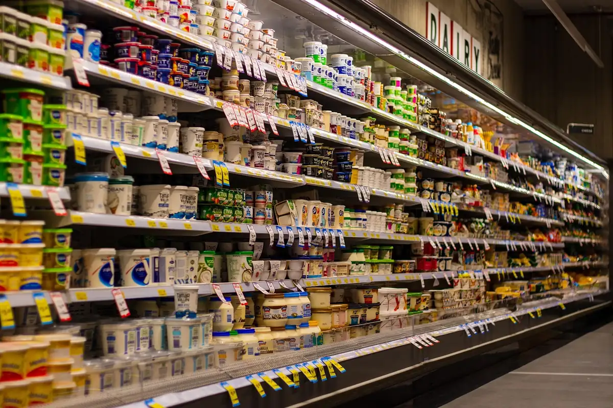 Rayon frais de supermarché rempli de pots de yaourt et de fromages blancs, étiquettes de prix jaunes