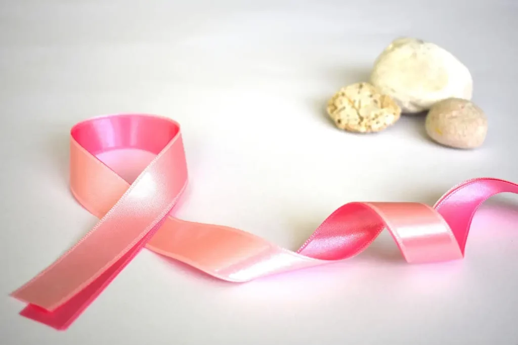 Ruban rose du dépistage du cancer du sein posé sur un fond blanc à côté de trois galets clairs