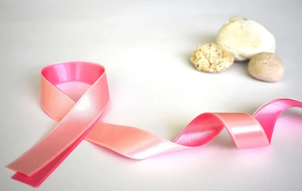 Ruban rose du dépistage du cancer du sein posé sur un fond blanc à côté de trois galets clairs