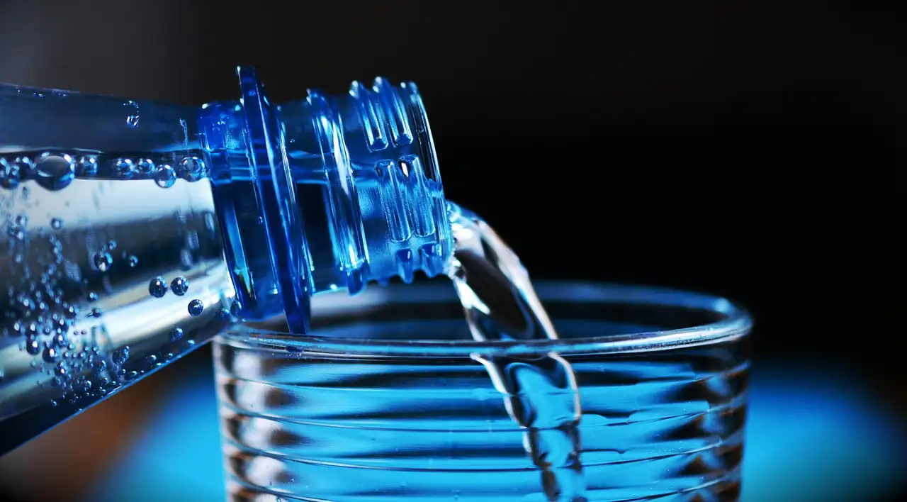 Bouteille d'eau minérale versée dans un verre posé sur fond sombre