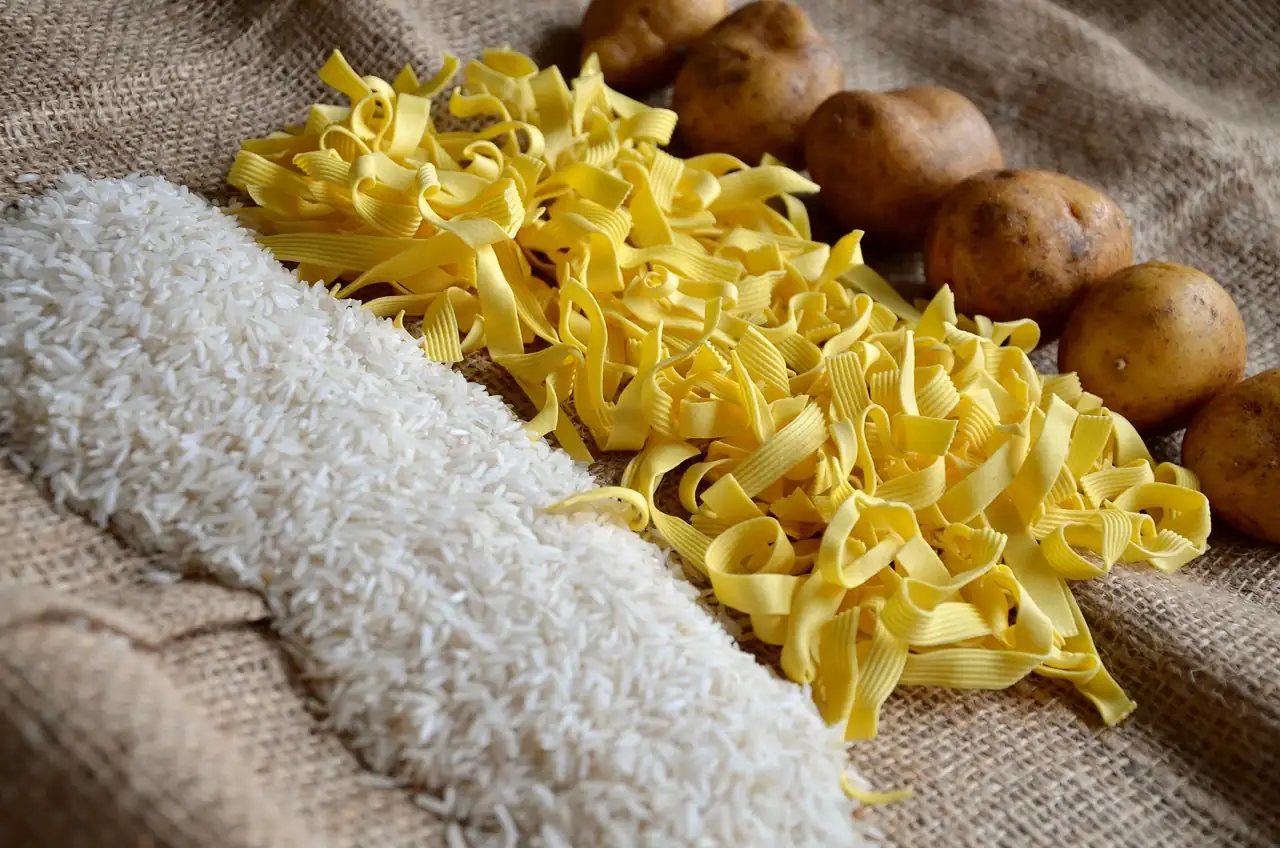 Riz, pâtes sèches et pommes de terre disposés côte à côte sur une toile de jute