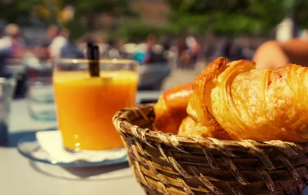 Corbeille de croissants et verre de jus d'orange sur une table en terrasse au soleil