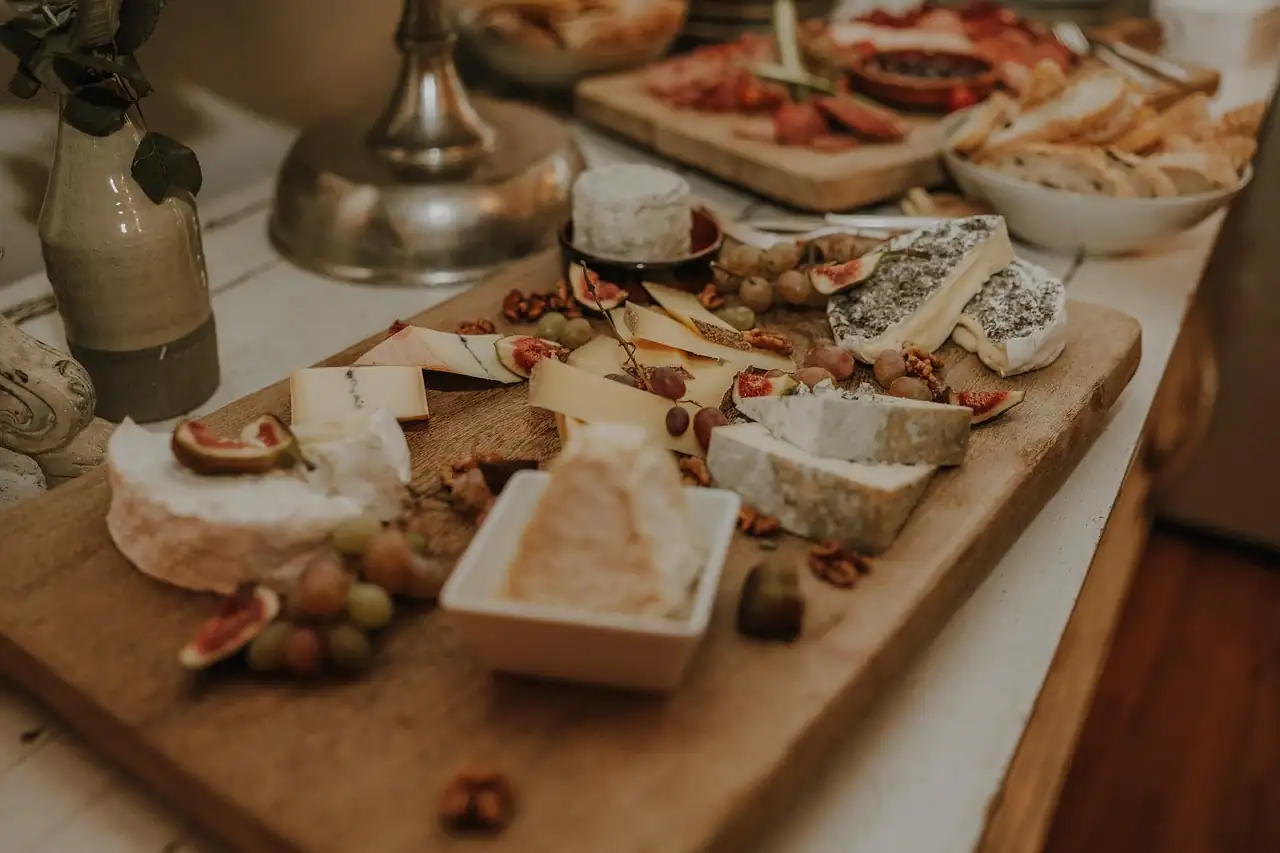 Planche en bois garnie de fromages, de charcuterie, de figues et de raisins, un bol de fromage frais au centre