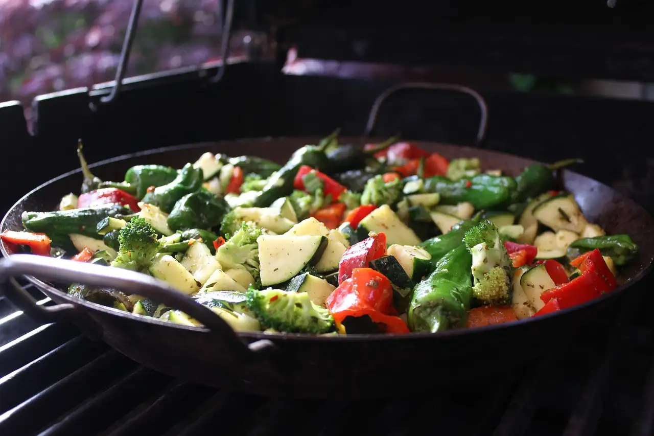 Poêle de courgettes, brocolis et poivrons grillés posée sur une grille de barbecue