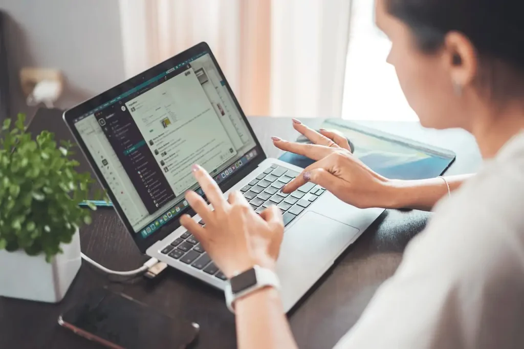 Femme assise à un bureau, mains sur le clavier d'un ordinateur portable, montre connectée au poignet