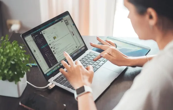Femme assise à un bureau, mains sur le clavier d'un ordinateur portable, montre connectée au poignet
