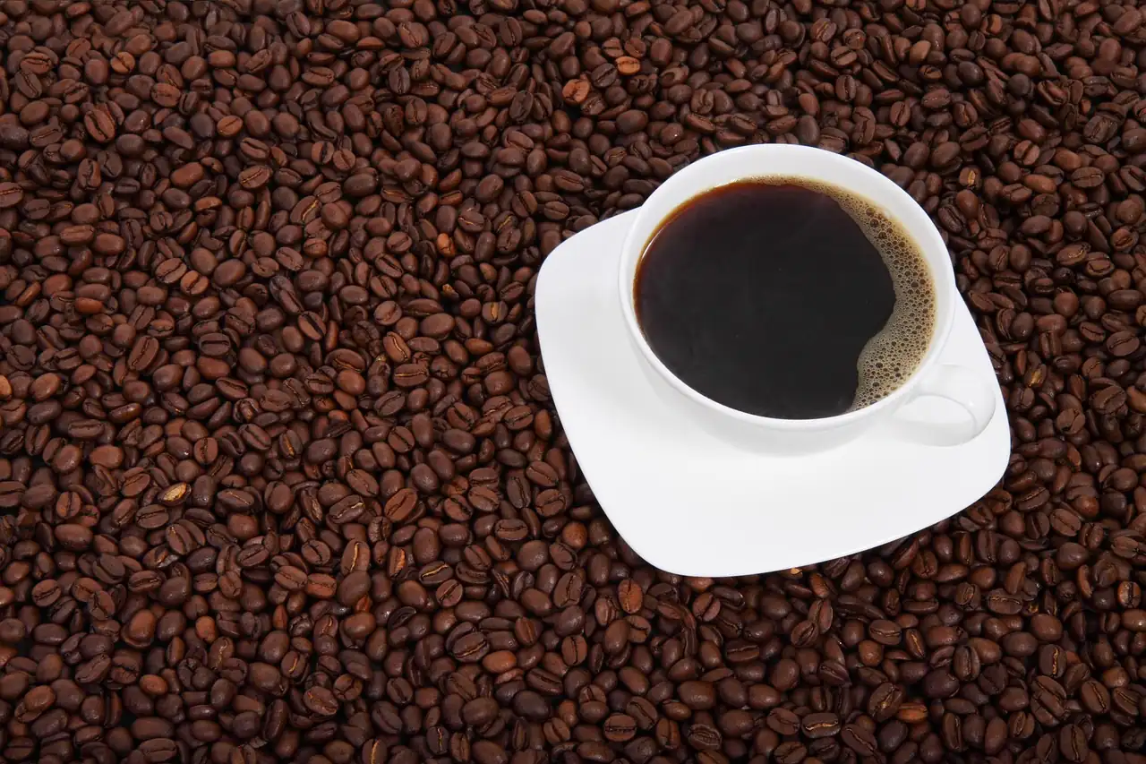 Tasse de café noir sur sa soucoupe blanche, posée sur un lit de grains de café torréfiés