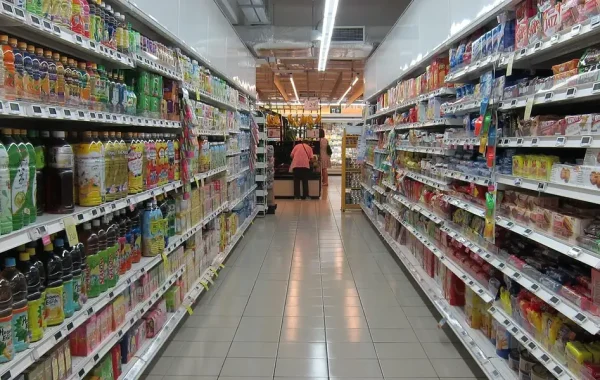 Allée de supermarché bordée de bouteilles de boissons et de paquets de biscuits sur plusieurs étagères