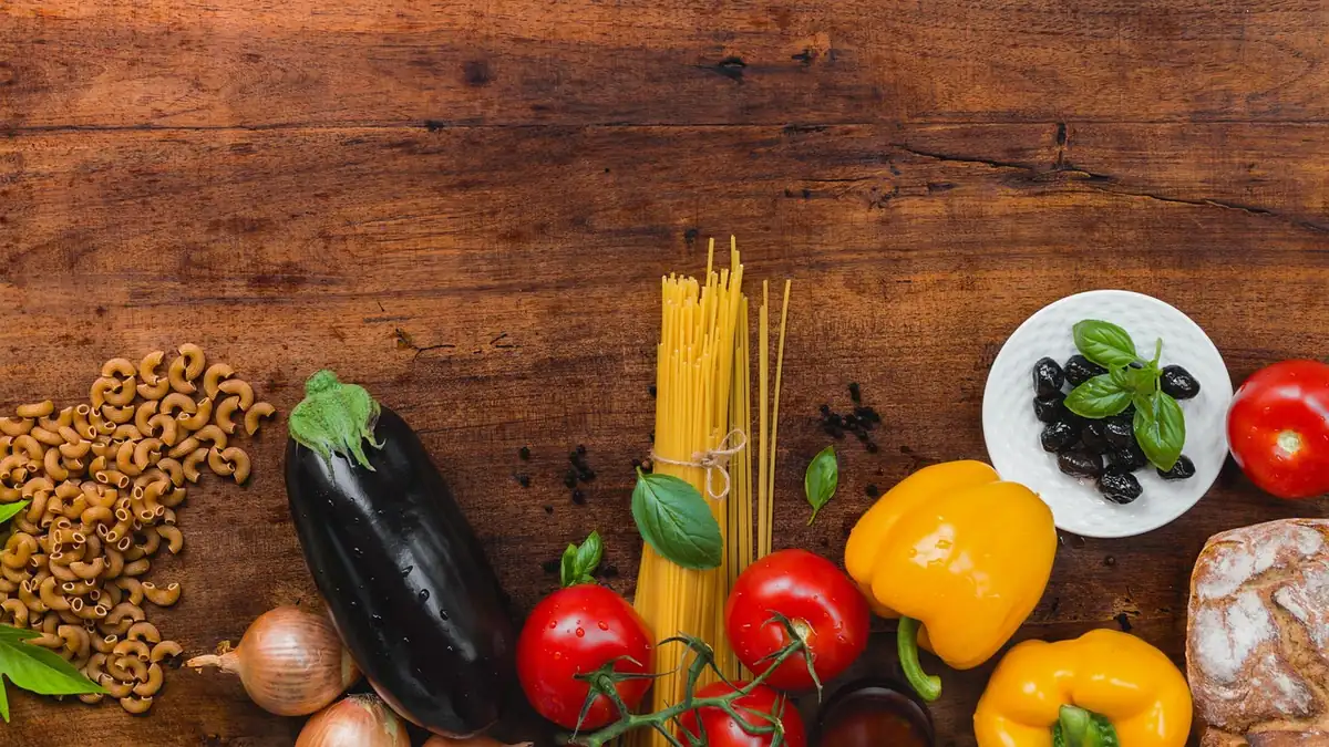 Pâtes sèches, aubergine, tomates, poivrons jaunes, olives et pain posés sur une table en bois