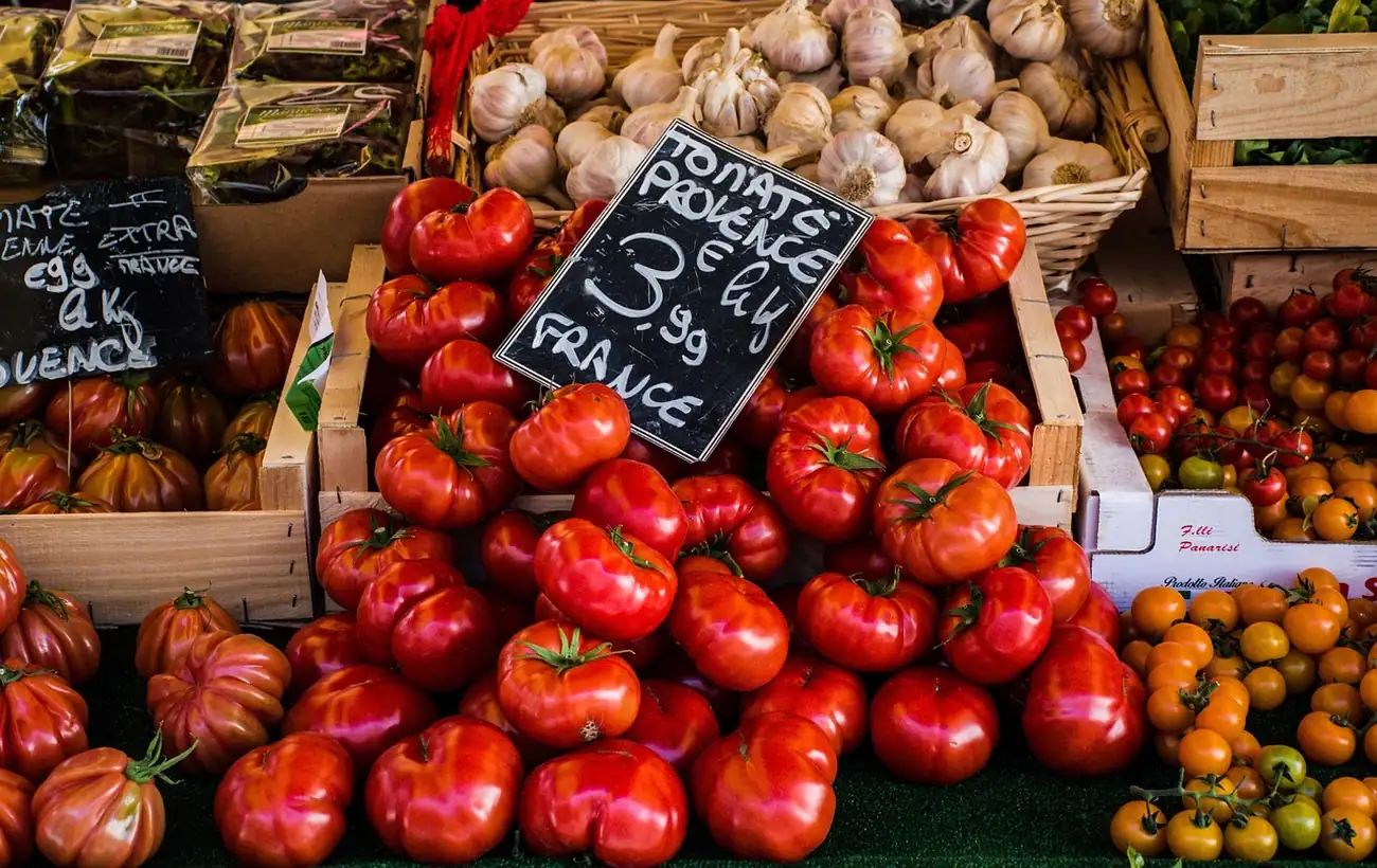 Étal de marché avec des tomates de Provence à 3,99 euros le kilo, des gousses d'ail et des cagettes en bois