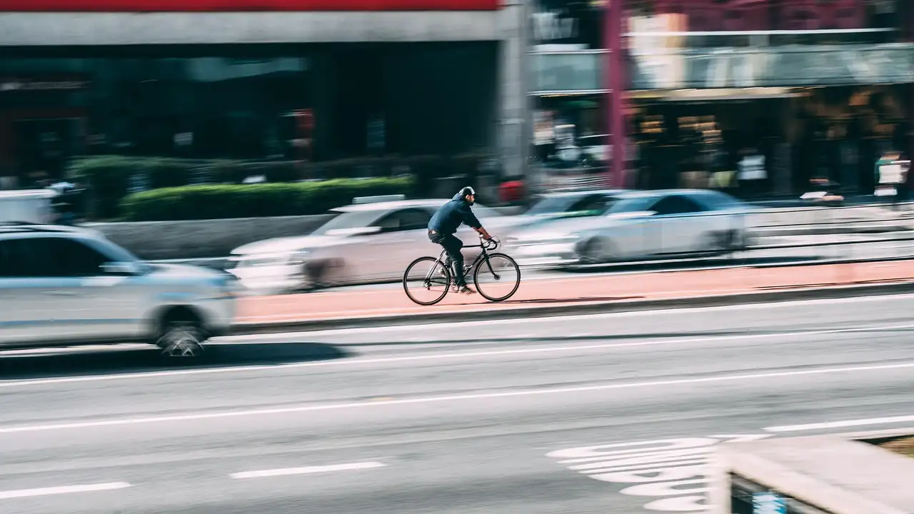 Cycliste seul sur une avenue, voitures floues qui le dépassent des deux côtés