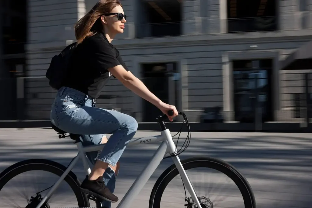 Jeune femme aux lunettes de soleil qui pédale sur un vélo blanc devant un immeuble de bureaux