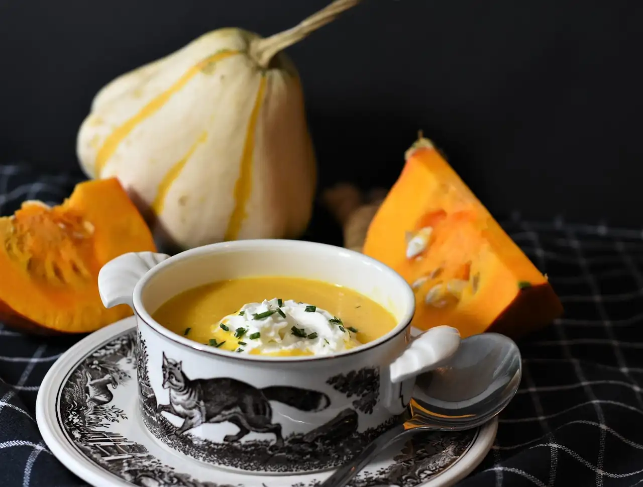 Tasse de velouté de potiron à la crème et à la ciboulette, entourée de morceaux de courge sur une nappe à carreaux