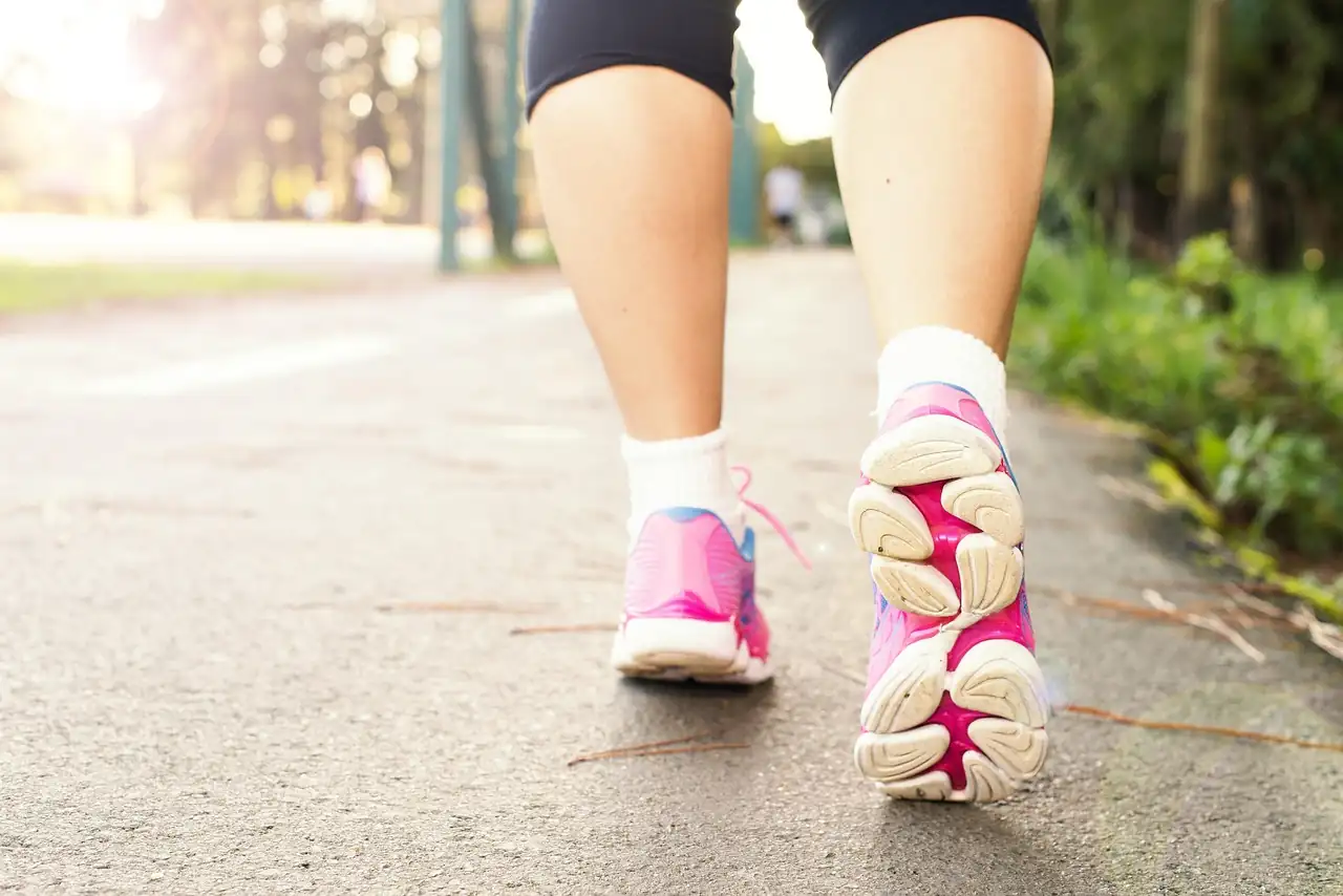 Gros plan sur des jambes en baskets roses qui marchent d'un bon pas sur un chemin goudronné