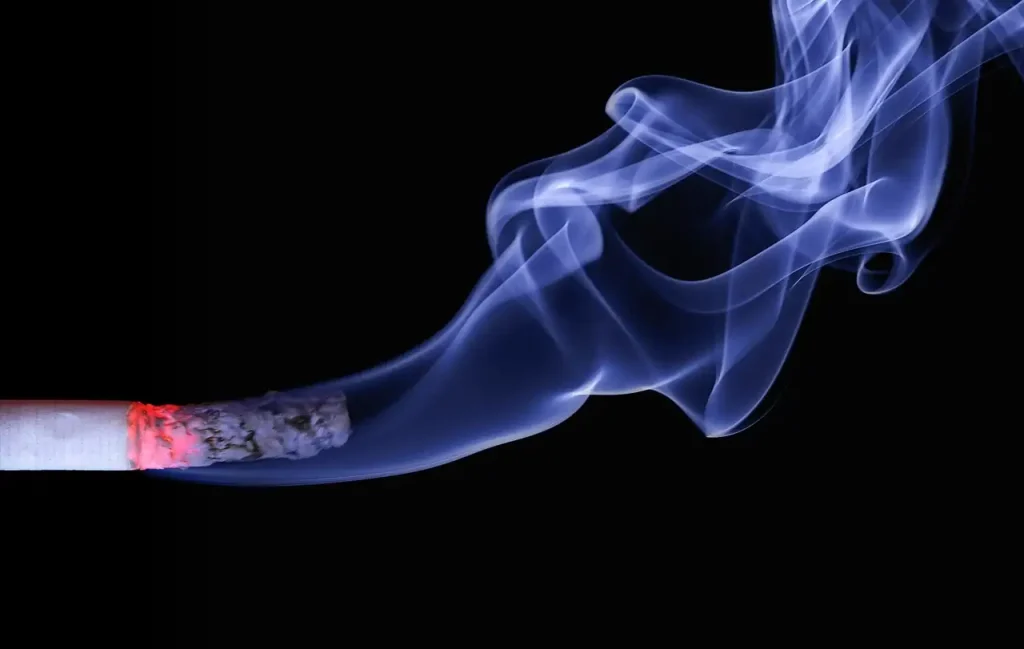 Cigarette allumée dont la fumée bleutée s'élève sur un fond noir