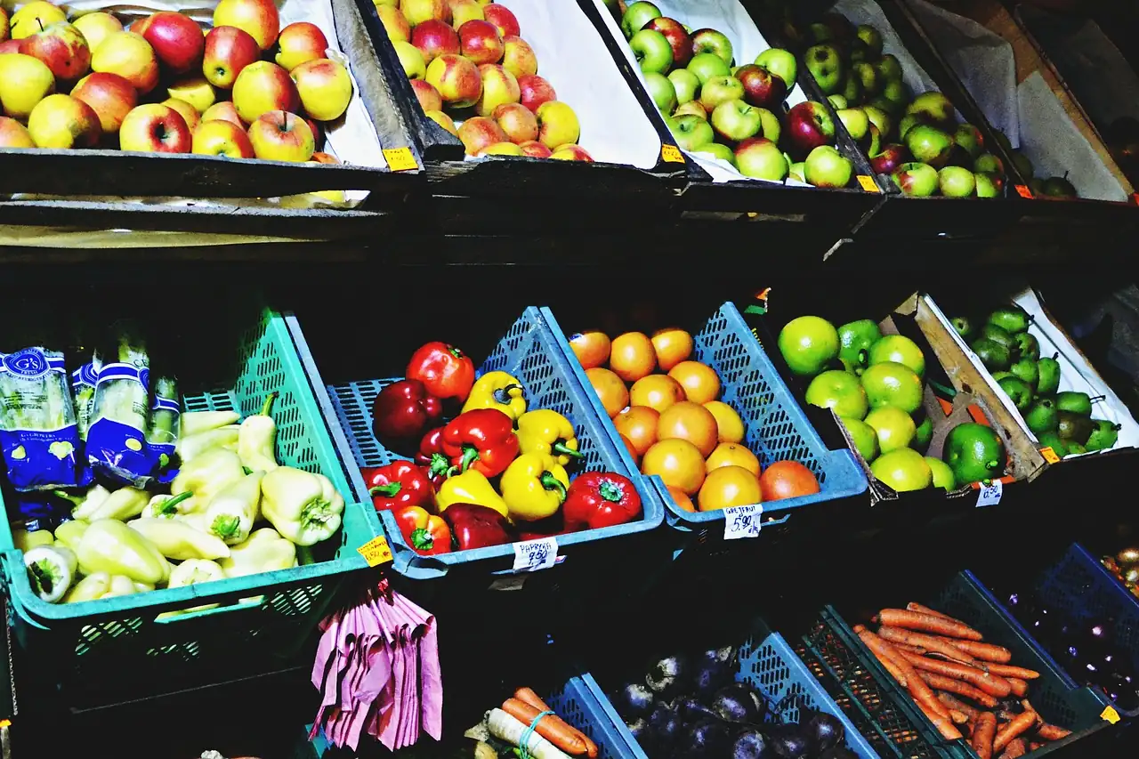 Étal de marché avec des cagettes de pommes, poivrons, oranges, citrons verts et carottes