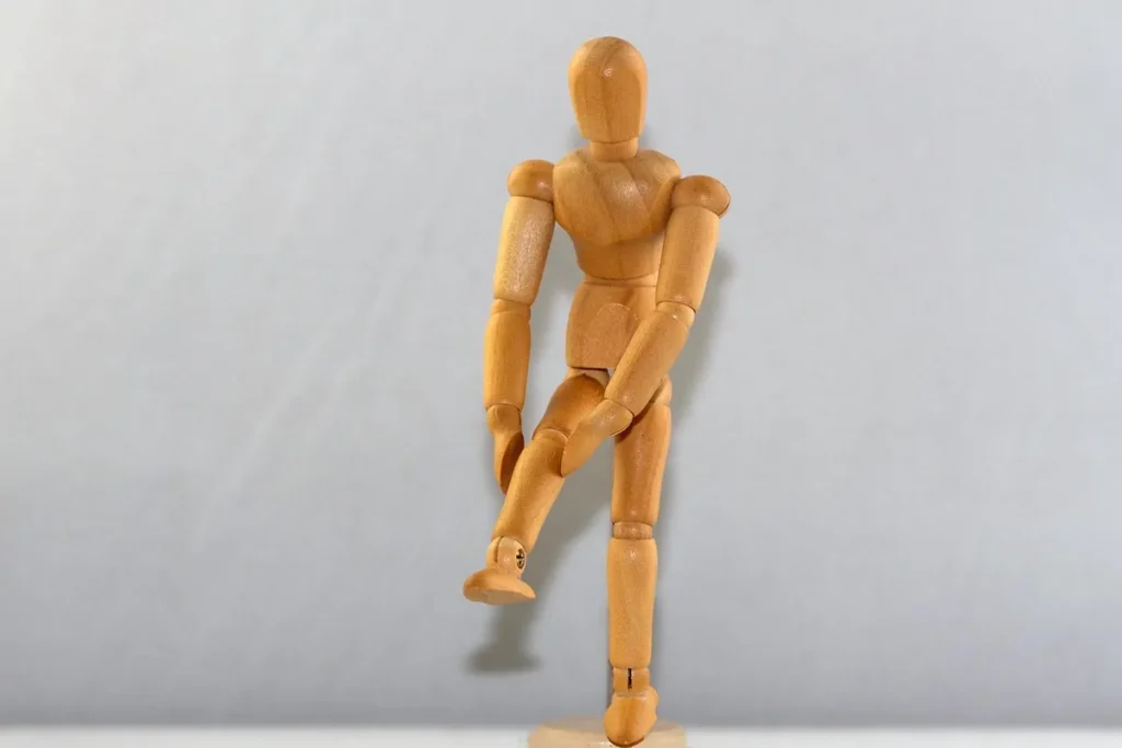 Mannequin articulé en bois debout sur une jambe, l'autre genou levé et tenu à deux mains