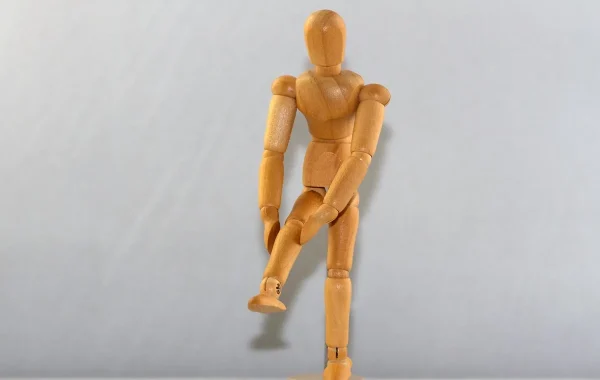 Mannequin articulé en bois debout sur une jambe, l'autre genou levé et tenu à deux mains