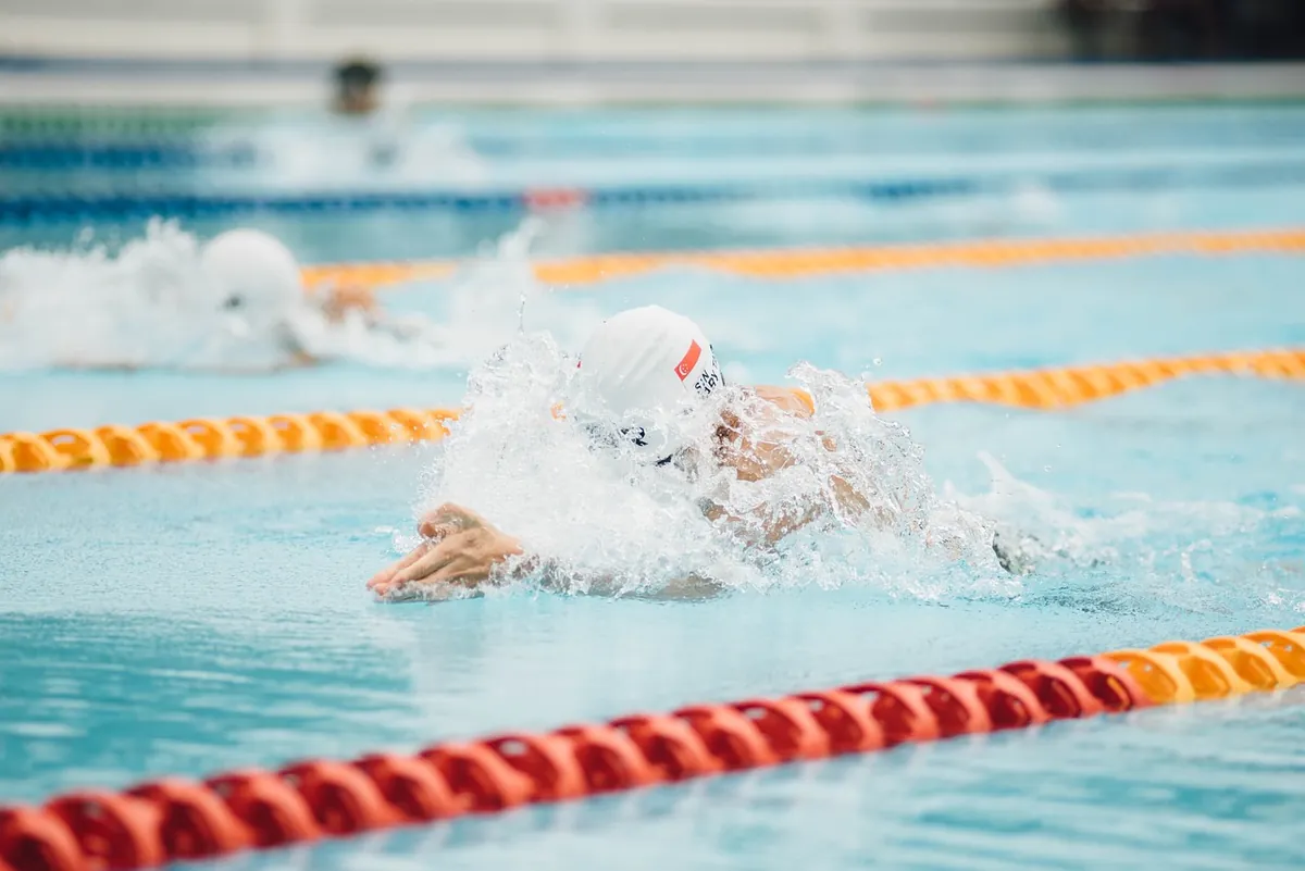 Nageur en bonnet blanc dans une piscine, entre deux lignes d'eau orange et rouges