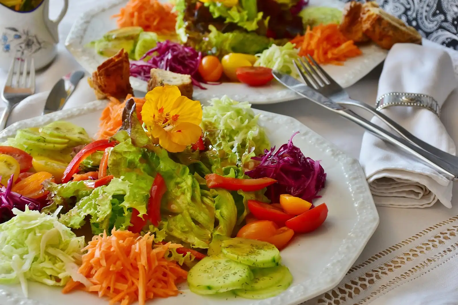 Assiette de crudités colorées : carottes râpées, chou rouge, tomates, concombre et une fleur jaune