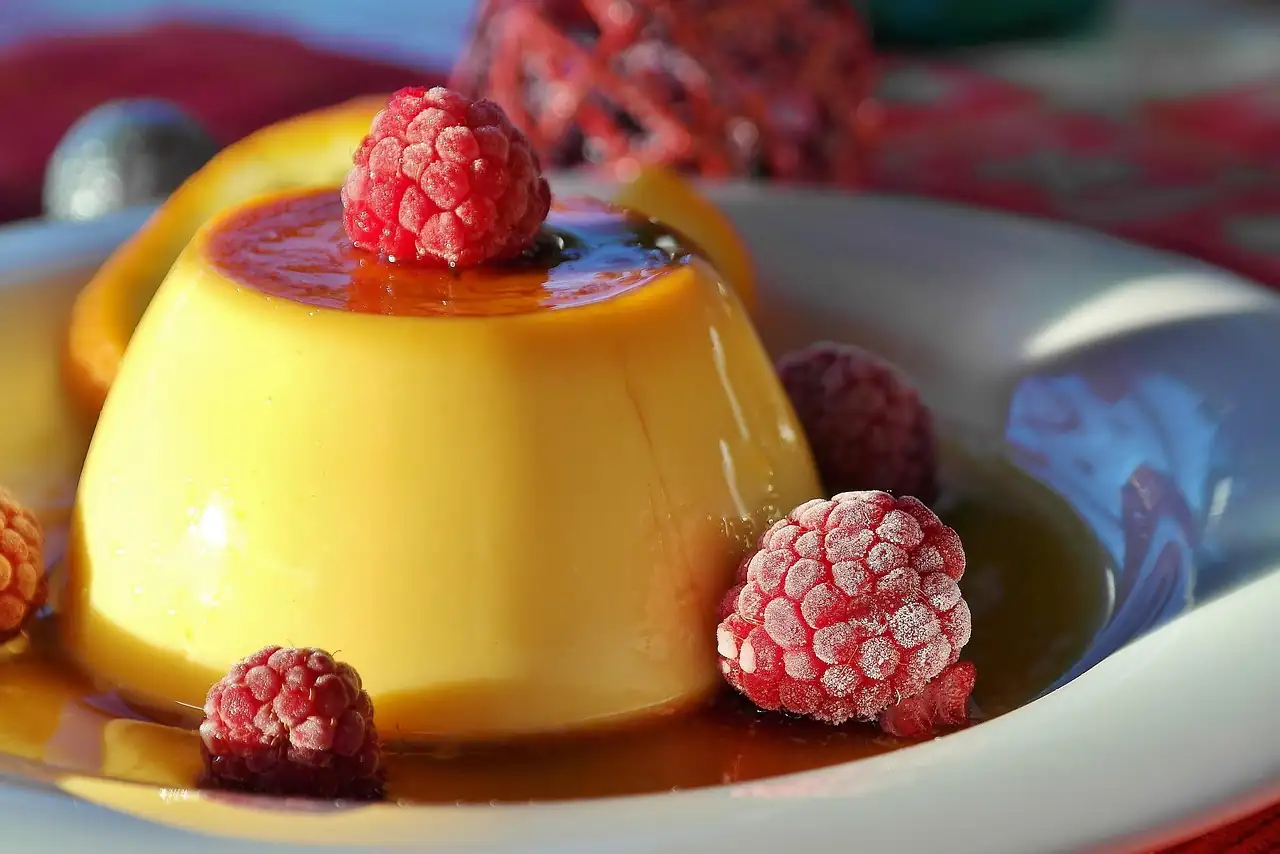 Flan à la vanille nappé de caramel, entouré de framboises givrées dans une assiette blanche