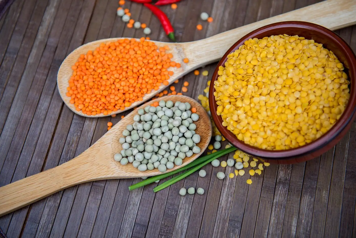 Lentilles corail, pois cassés verts et lentilles jaunes dans des cuillères en bois et un bol sur une table