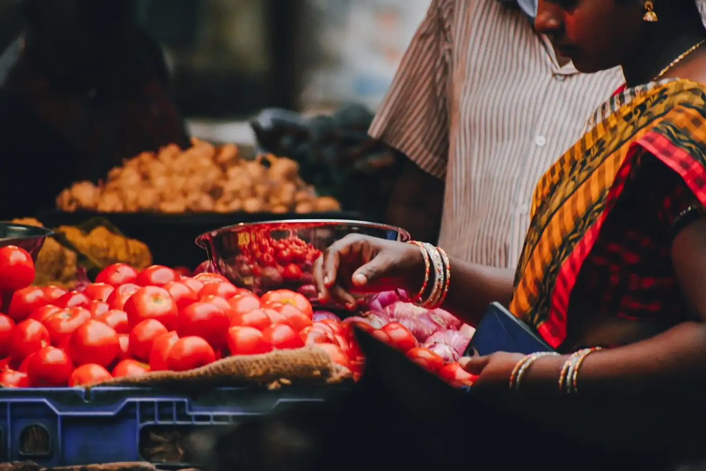 Femme en sari qui trie des tomates rouges sur un étal de marché, des oignons en arrière-plan
