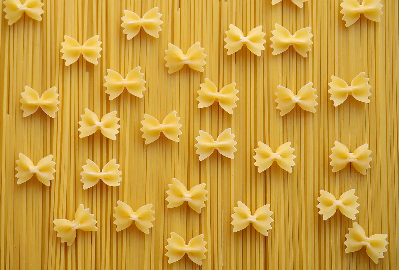 Pâtes crues en forme de nœud papillon posées sur un lit de spaghetti secs