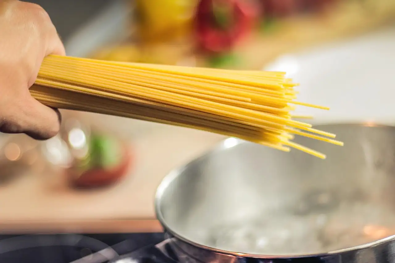 Main qui tient une poignée de spaghetti secs au-dessus d'une casserole d'eau sur le feu