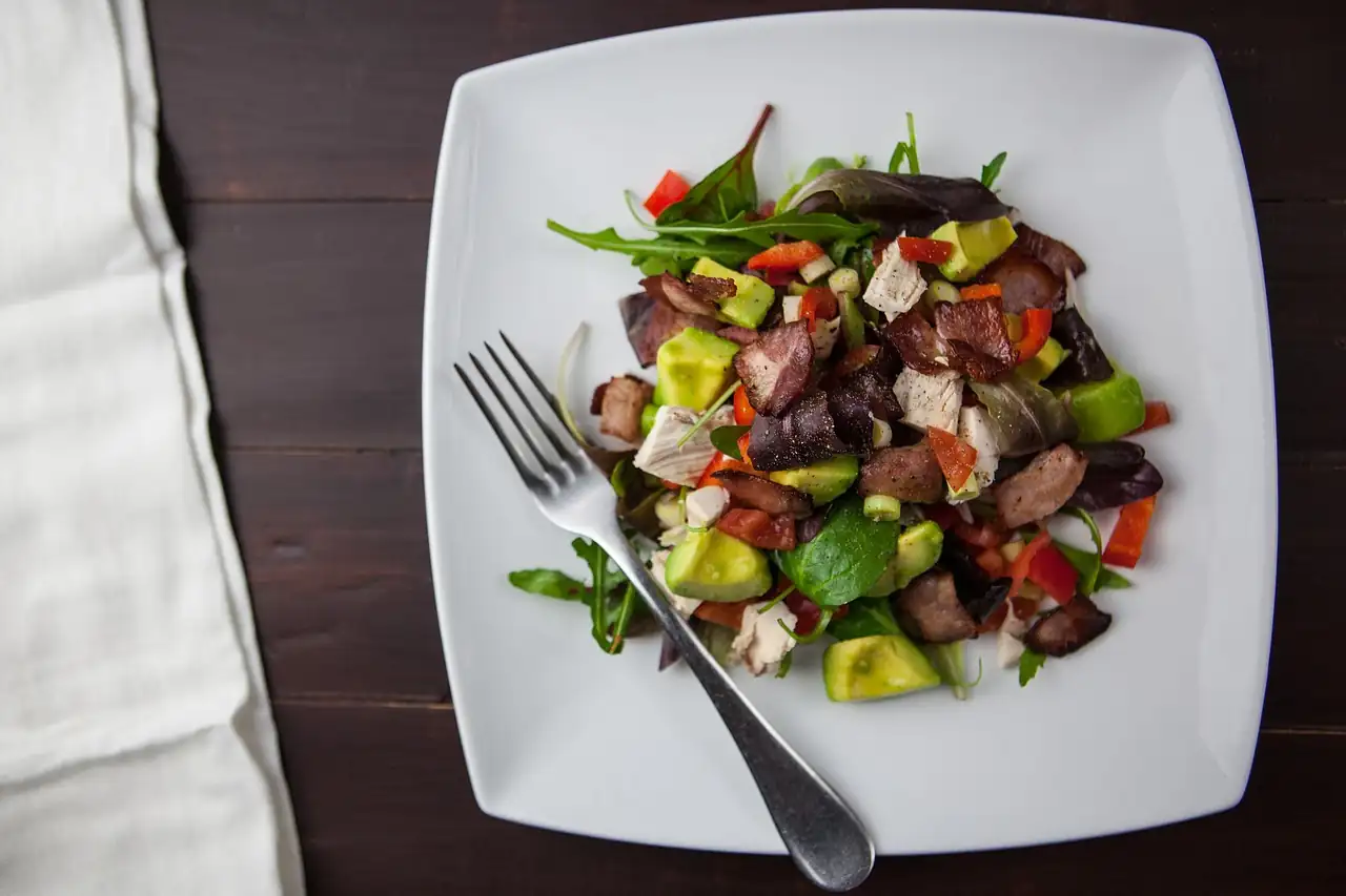 Assiette carrée blanche de salade à l'avocat, poulet et poivron, une fourchette posée dessus