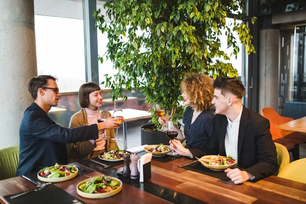 Quatre amis trinquent autour d'une table de restaurant garnie d'assiettes de salade composée