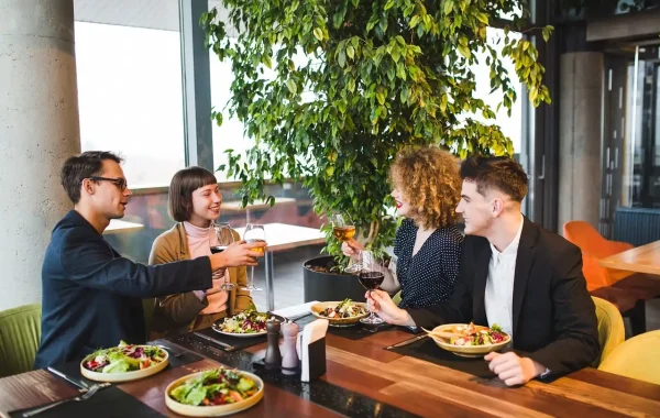 Quatre amis trinquent autour d'une table de restaurant garnie d'assiettes de salade composée