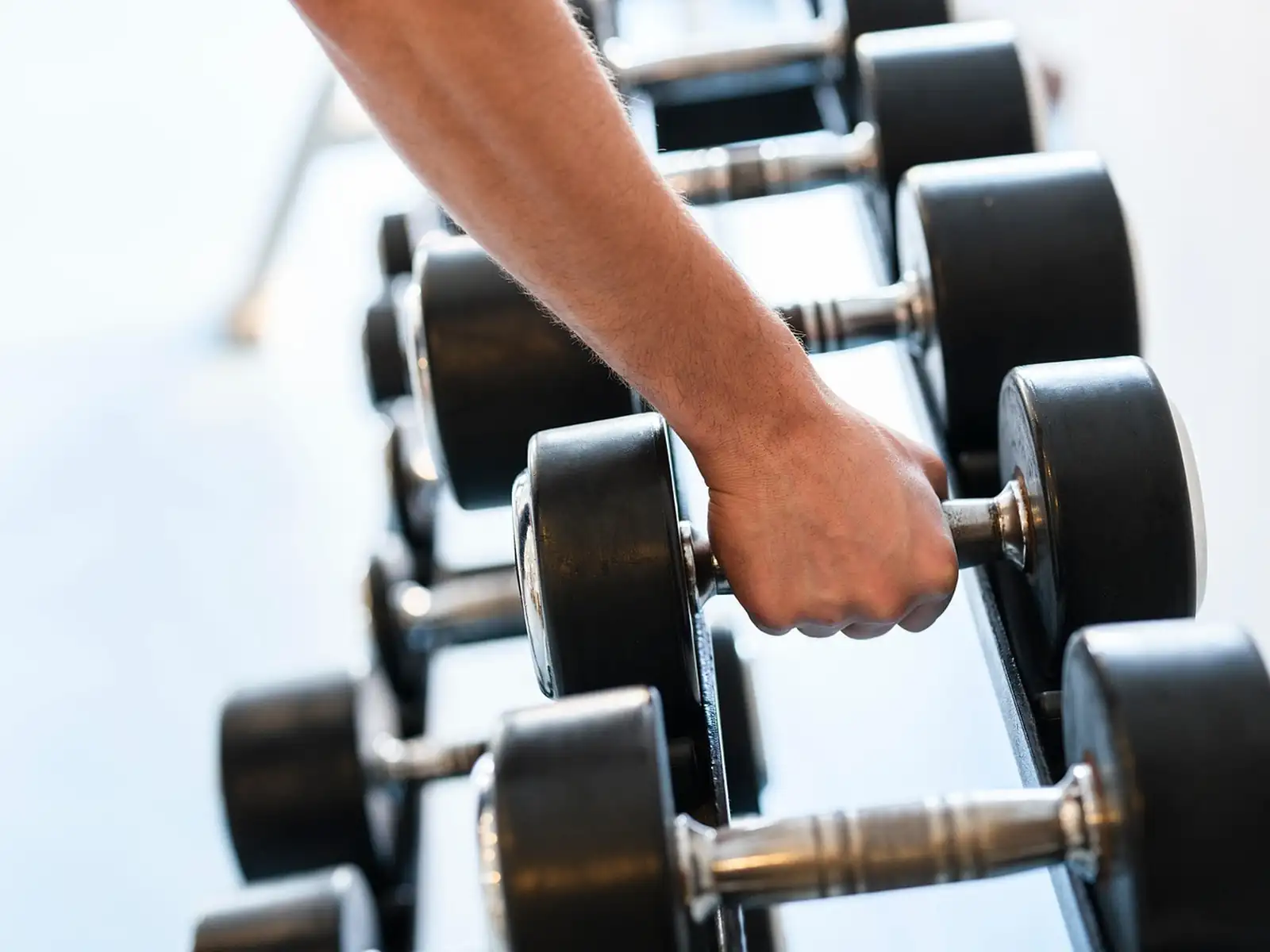 Main qui saisit un haltère noir sur un rack d'haltères dans une salle de sport lumineuse