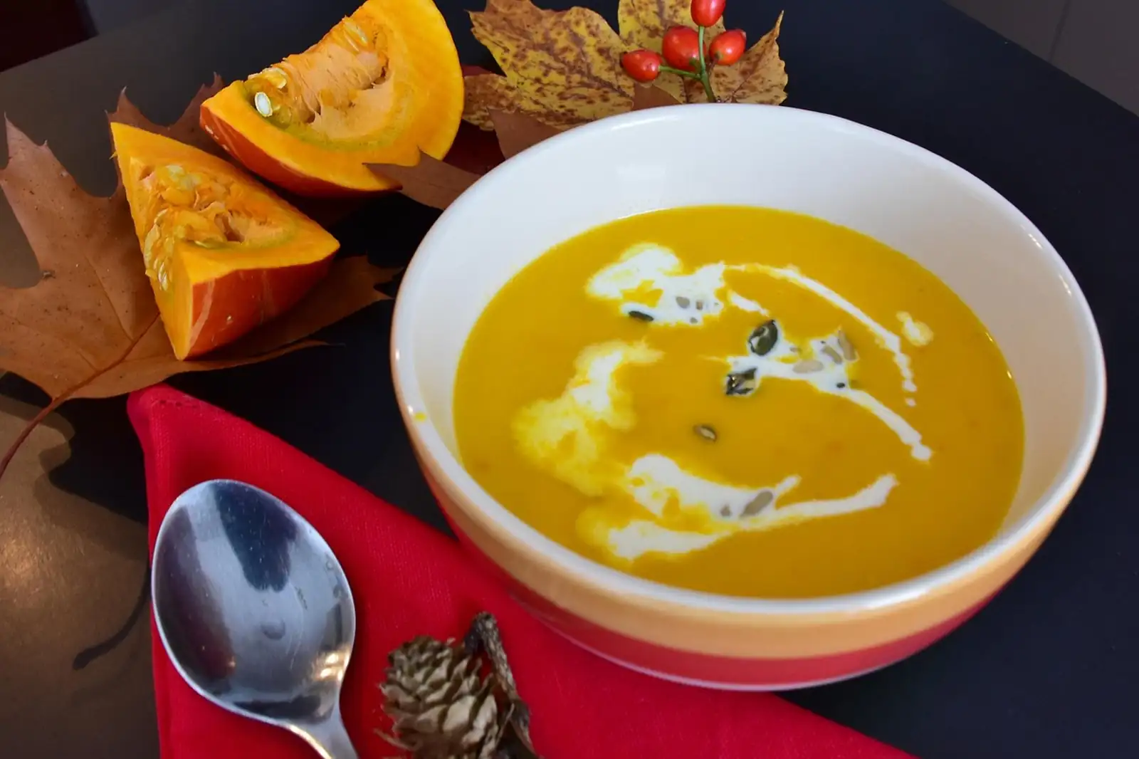 Bol de velouté de potiron avec un trait de crème, quartiers de potiron et feuilles d'automne autour