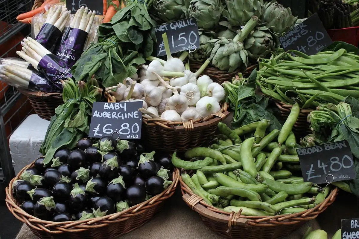 Étal de marché avec paniers d'aubergines, d'ail frais, de fèves, d'artichauts et d'asperges blanches