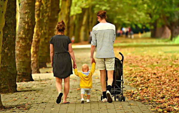 Couple de dos qui tient la main d'un jeune enfant en sweat jaune, allée de platanes et feuilles mortes