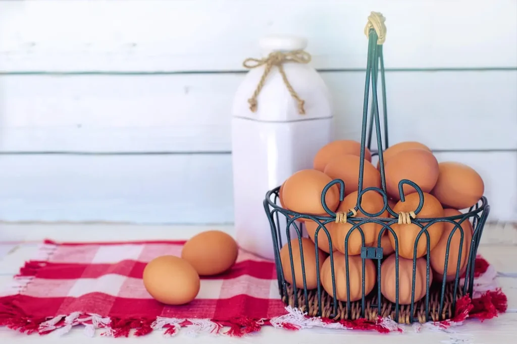 Panier en métal rempli d'œufs bruns posé sur un torchon à carreaux rouges, à côté d'une bouteille de lait